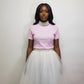 Woman wearing a pink t shirt with a rhinestone text and a white tulle skirt against a plain background